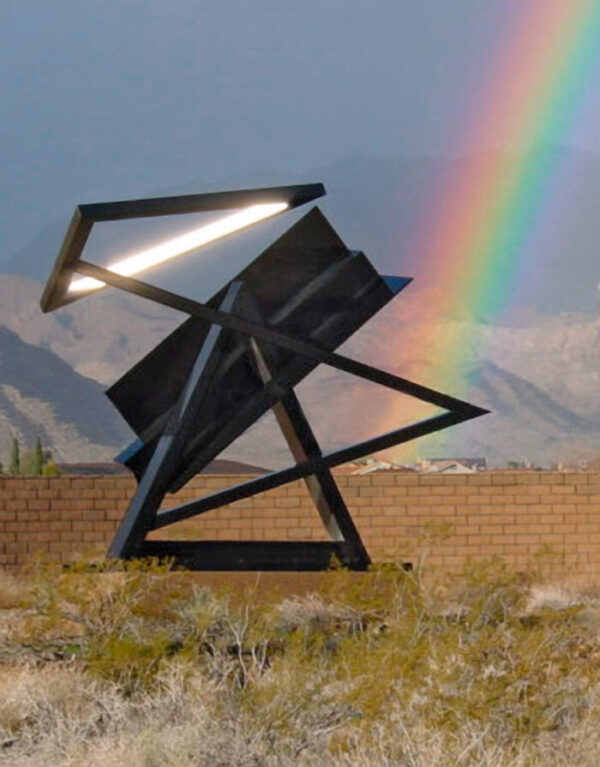 Holocaust, 1998-2000, a steel sculpture created by Rita Deanin Abbey. Two triangles, symbolizing the Star of David, comprise the main sections of this sculpture. The base triangle is interrupted by the mass of a stepped plane. The arm, emerging from the base triangle, connects the displaced second triangle of the Star. The sculpture sits in the outdoor sculpture garden at the Rita Deanin Abbey Art Museum, surrounded by desert plant life and mountains. A rainbow shines in the background of the photo.