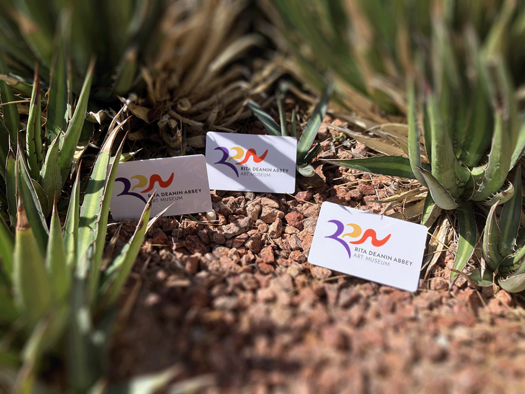 Three white membership cards with the museum logo sit in landscaping rocks surrounded by desert shrubbery.