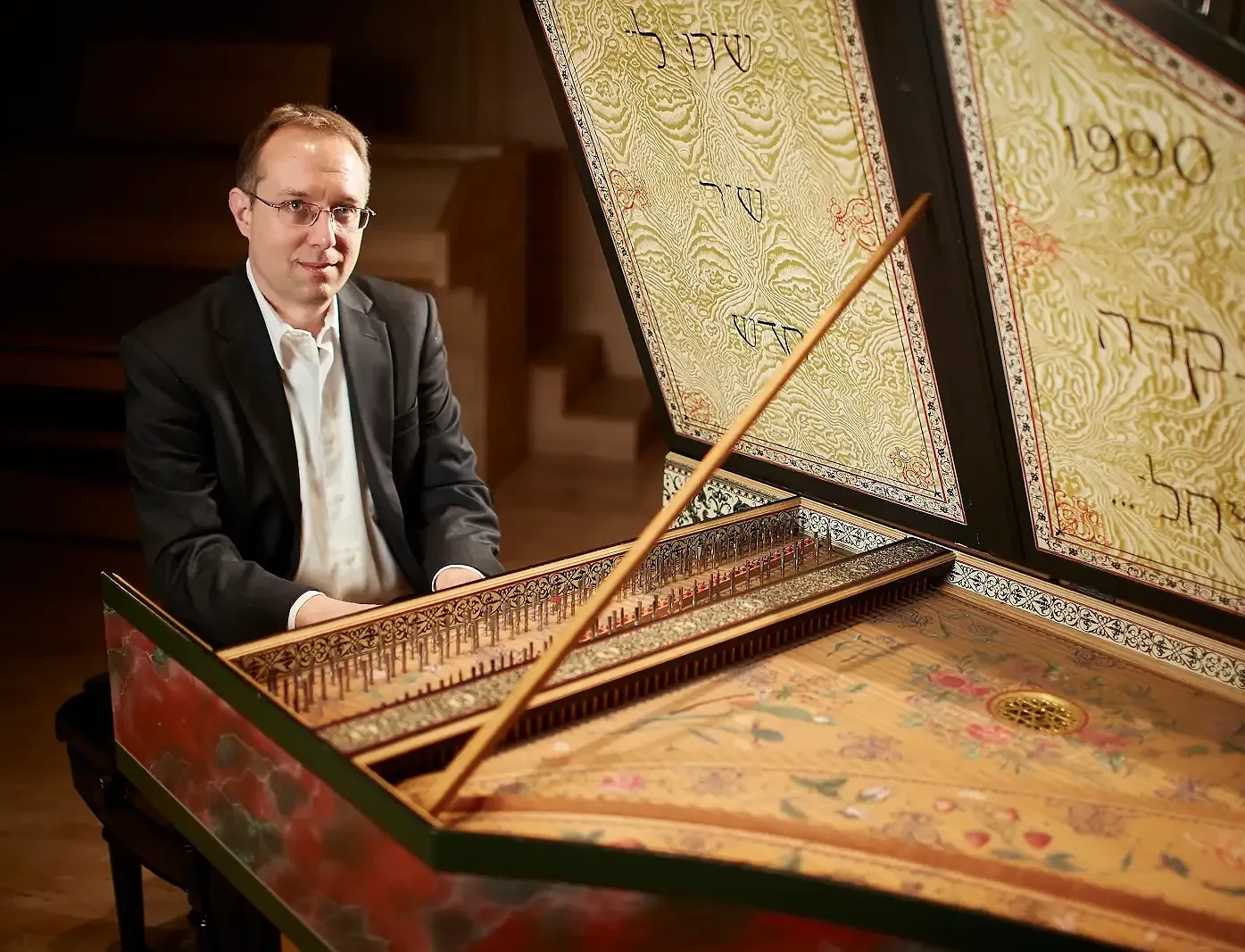 Professional photo of a man, Johnathan Rhodes Lee, playing his Harpsichord and smiling at the camera