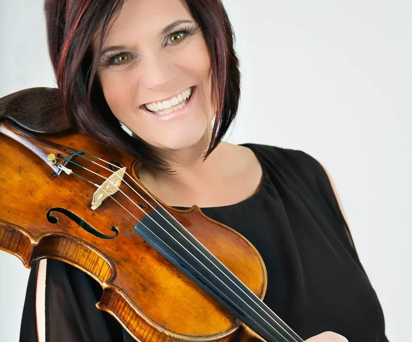 Headshot of a smiling woman, DeAnn Letourneau, holding a violin on her shoulder against a white background.