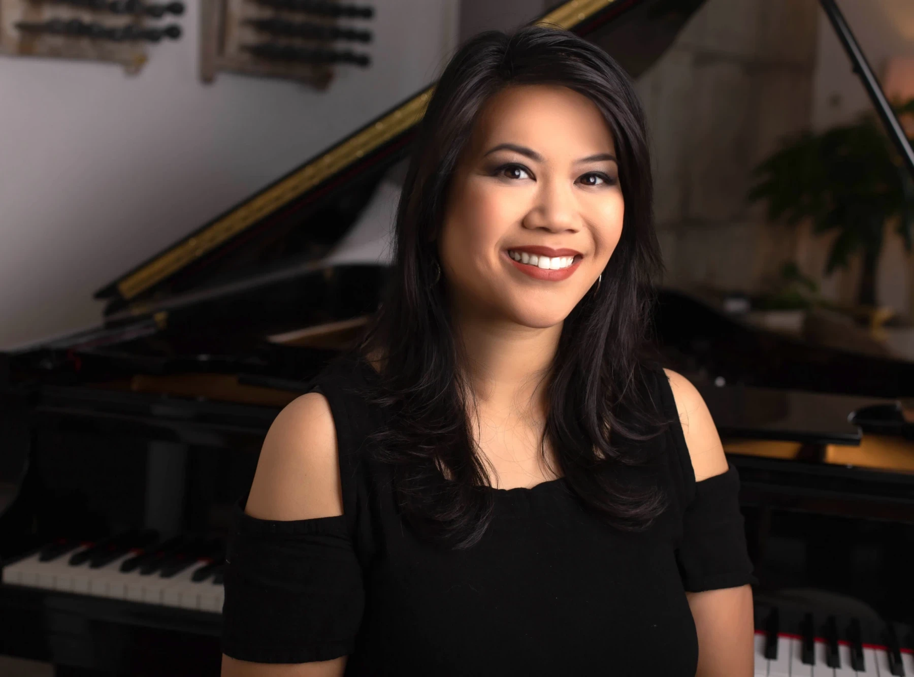 A smiling woman, Alexandria Le, smiling for a portrait photo with her piano behind her. The photo was taken indoors.