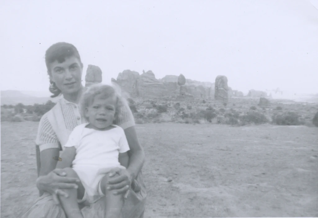 Rita holding baby Joshua in her lap in front of the Arches in Moab, Utah. Both are looking at the camera, Rita gives a small smile, while baby Joshua looks stressed.