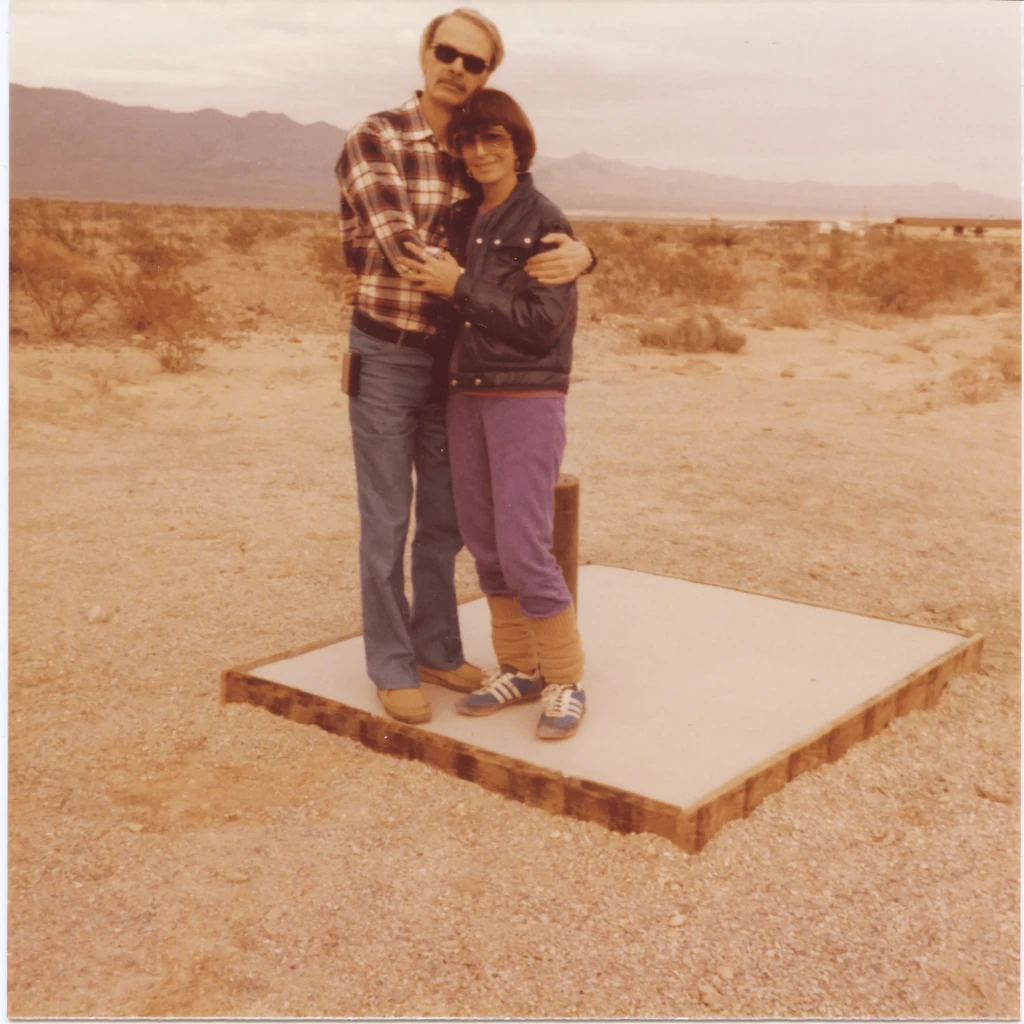 Robert (left) and Rita (right) in a warm embrace, facing the camera and standing on a platform, which would later become their home in the desert.