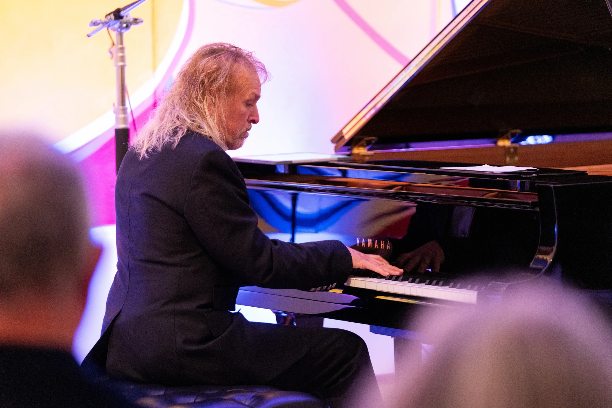 Philip Fortunbery playing piano in front of an audience, sitting with the piano to the right of frame